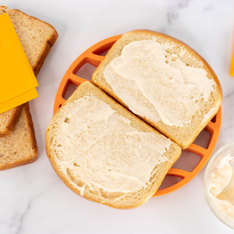 Softened butter spread edge to edge on sandwich bread for grilled cheese preparation