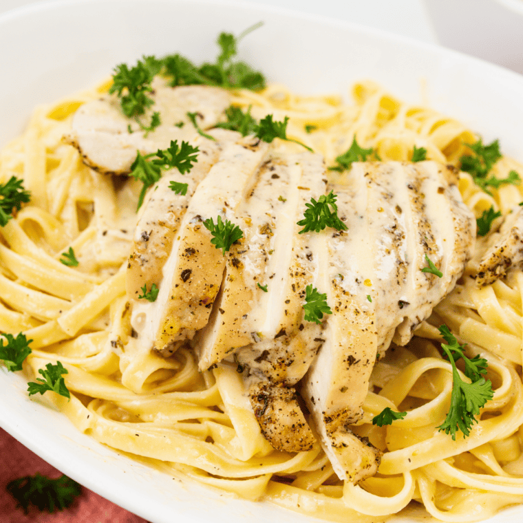 Bowl of creamy alfredo pasta topped with sliced chicken and parmesan cheese.