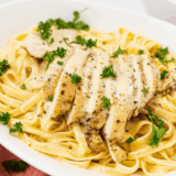 Creamy chicken alfredo pasta with sliced chicken breast in a white bowl.