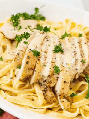 Creamy chicken alfredo pasta with sliced chicken breast in a white bowl.