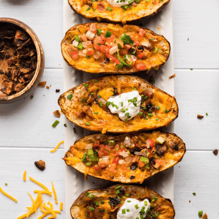 Air fryer Texas Roadhouse-style tater skins topped with cheese, bacon, and green onions on a serving plate.