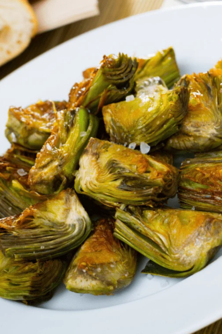 Crispy golden air fryer frozen artichokes on a white plate with a lemon wedge and dipping sauce