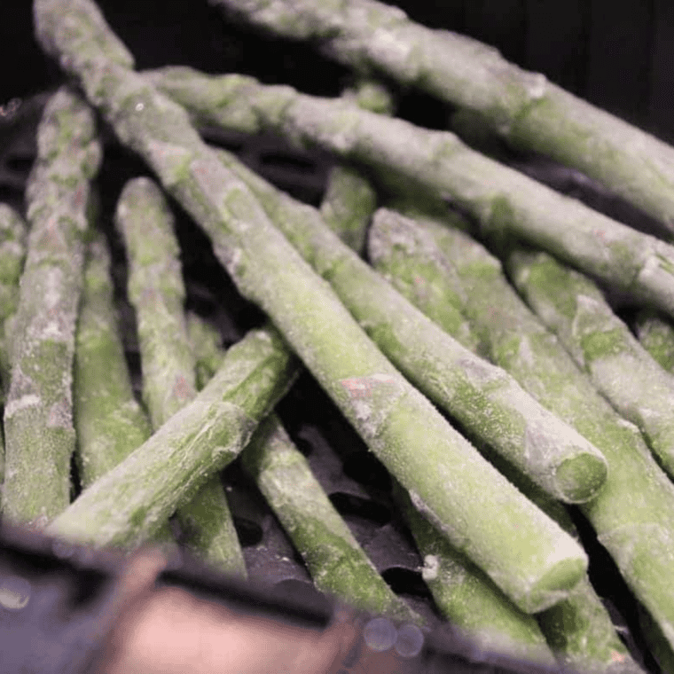 Frozen asparagus placed in the air fryer basket for even cooking without thawing.