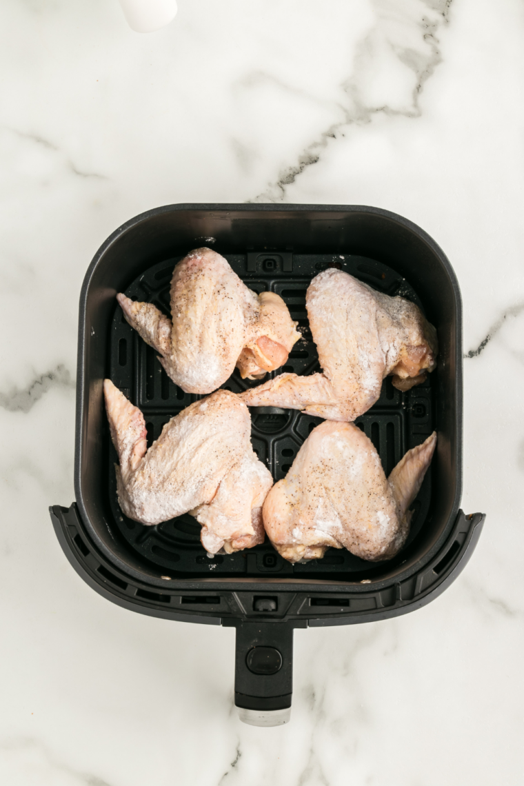 Raw seasoned wings arranged in a single layer inside an air fryer basket, cooking until golden and crispy.