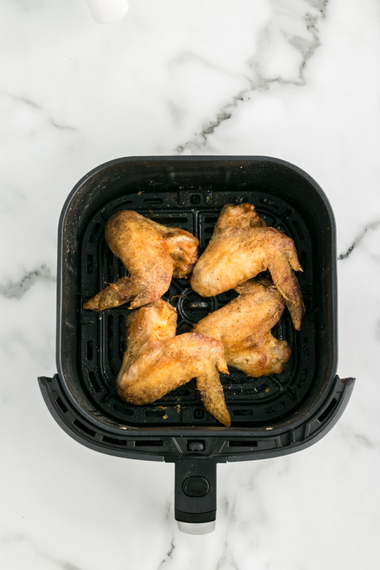 Cooked crispy chicken wings being tossed in a bowl of sticky honey BBQ sauce until fully coated.