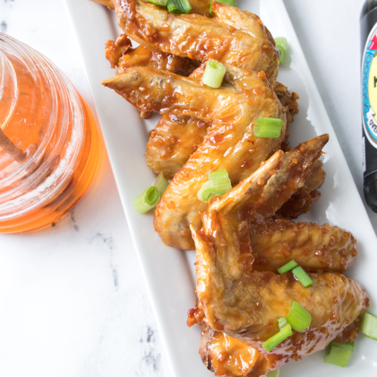 A plate of crispy air fryer honey garlic chicken wings coated in a glossy, sweet, and savory sauce, garnished with sesame seeds and green onions.