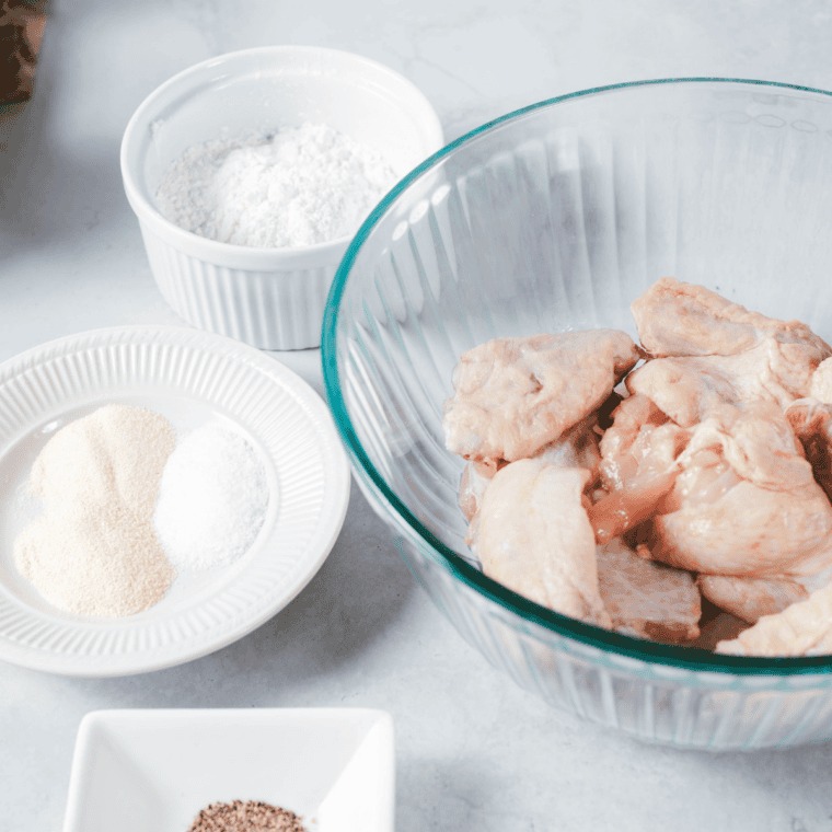 Raw chicken wings in the bowl with the spices next to them on a counter.