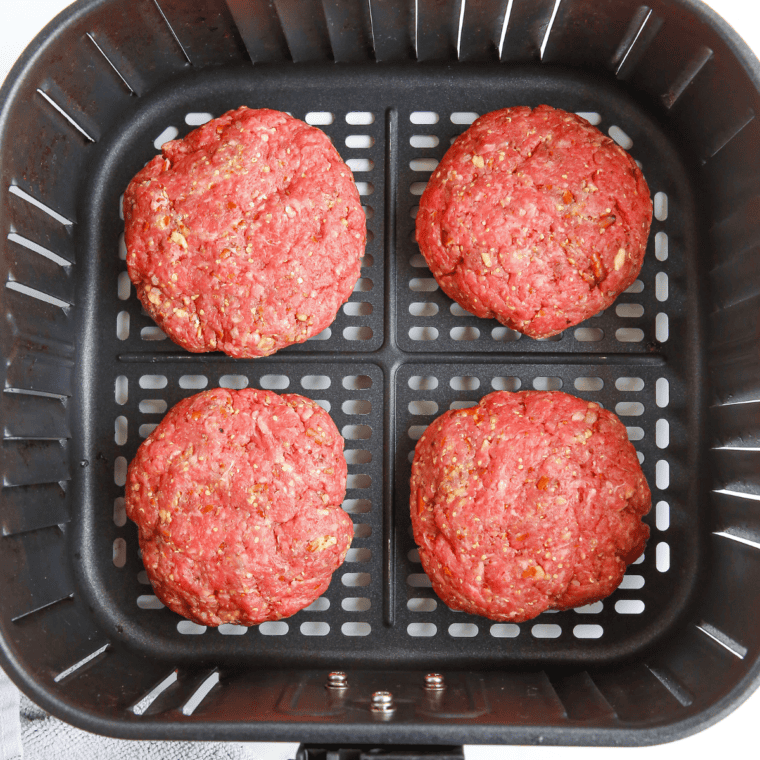 Raw burgers in the air fryer basket.