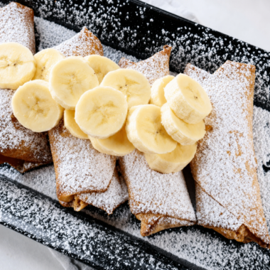Crispy air fryer peanut butter banana egg rolls dusted with powdered sugar on a white plate