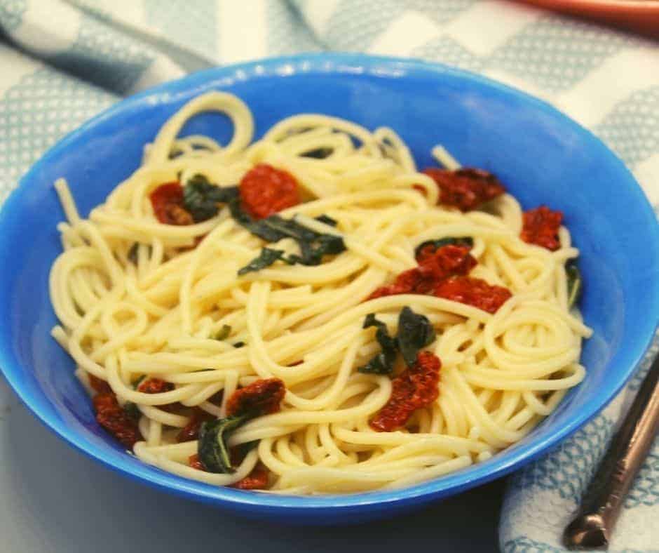 closeup: a blue bowl full of spaghetti with air fryer sun dried tomatoes and spinach