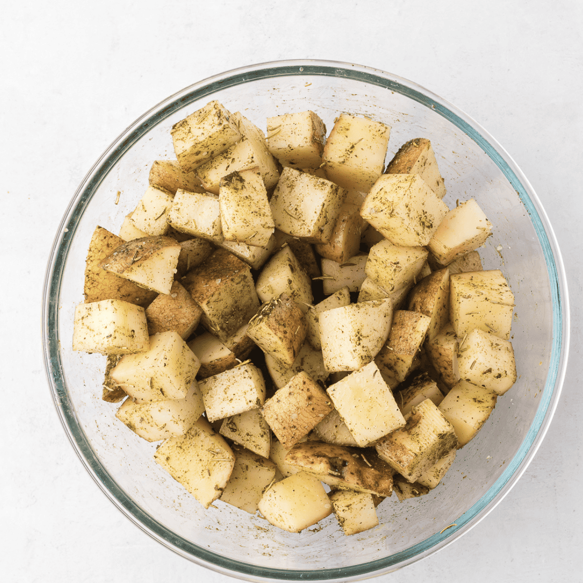 Tossing diced potatoes with olive oil, rosemary, thyme, salt, and pepper in a large mixing bowl.