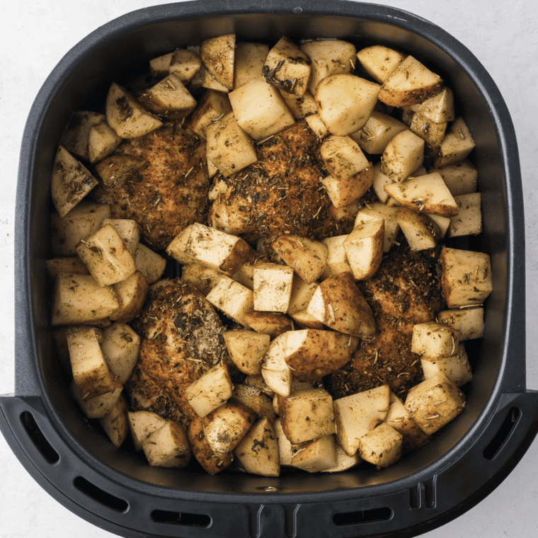 Adding seasoned potatoes to air fryer basket with chicken, cooking until golden and fully cooked through.