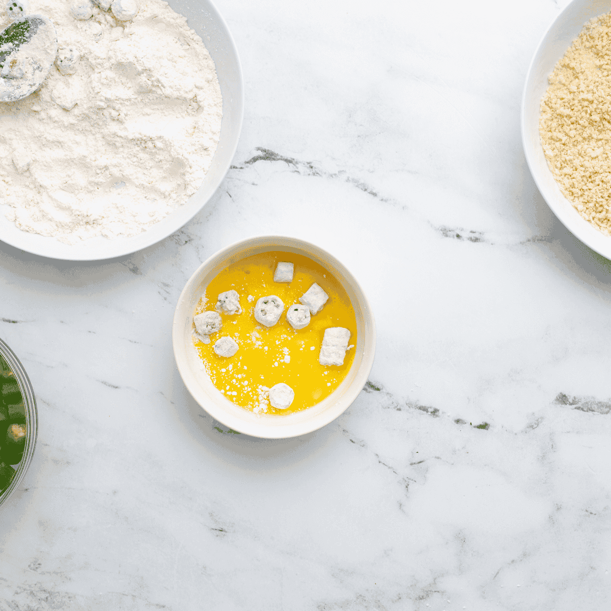 Preparing the breading station with flour in a small bowl, whisked eggs in a shallow bowl, and breadcrumbs in a mixing bowl.