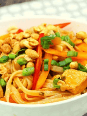 Bowl of Ninja Foodi chicken pad thai topped with crushed peanuts, sliced scallions, and a lime wedge