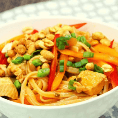 Bowl of Ninja Foodi chicken pad thai topped with crushed peanuts, sliced scallions, and a lime wedge