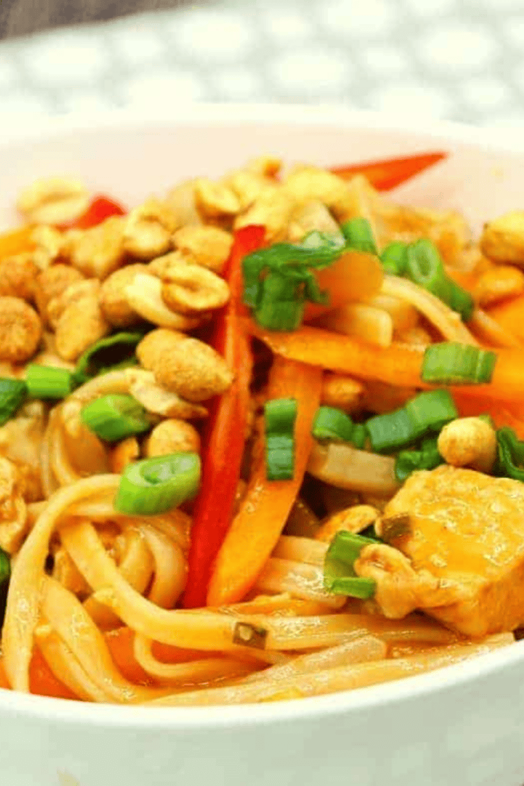 Bowl of Ninja Foodi chicken pad thai topped with crushed peanuts, sliced scallions, and a lime wedge