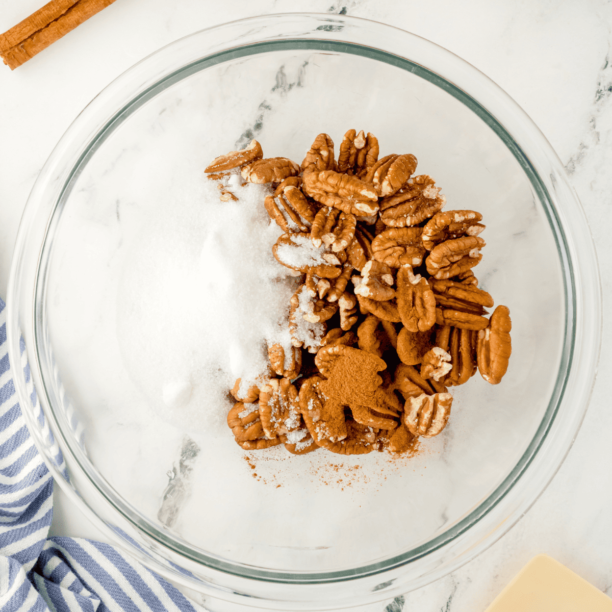 overhead process shot: pecans, sugar, and cinnamon in a large glass bowl before mixing