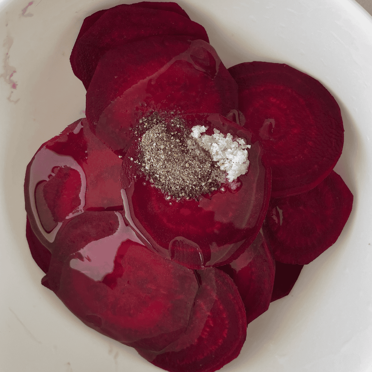 Sliced beets in a bowl, drizzled with olive oil and sprinkled with salt.