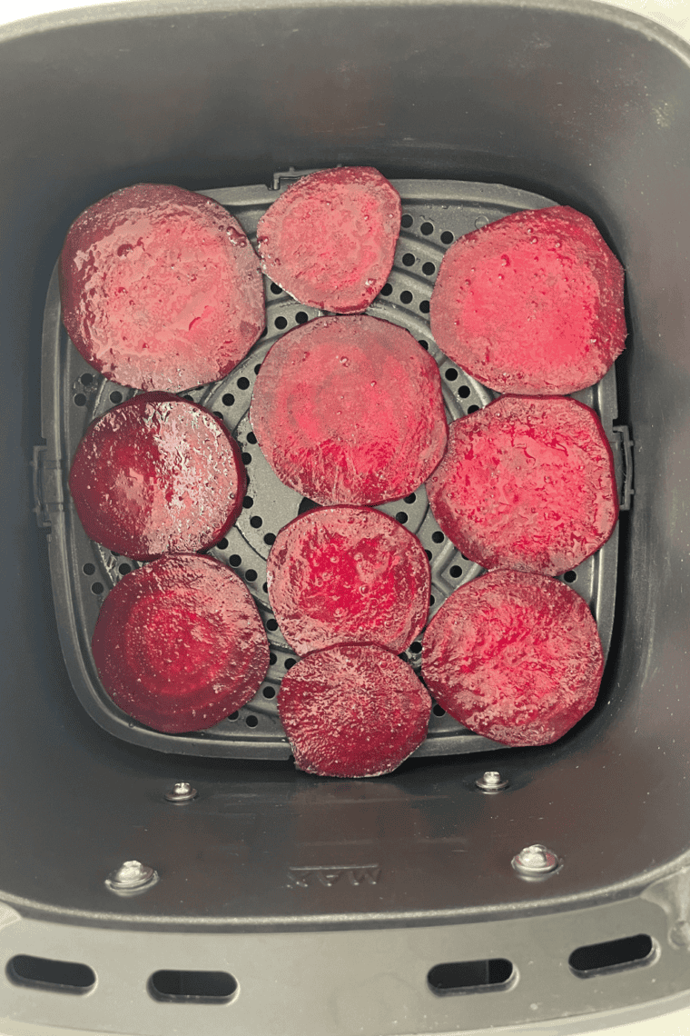 Seasoned beet slices spread in a single layer in the air fryer basket, ready to cook.