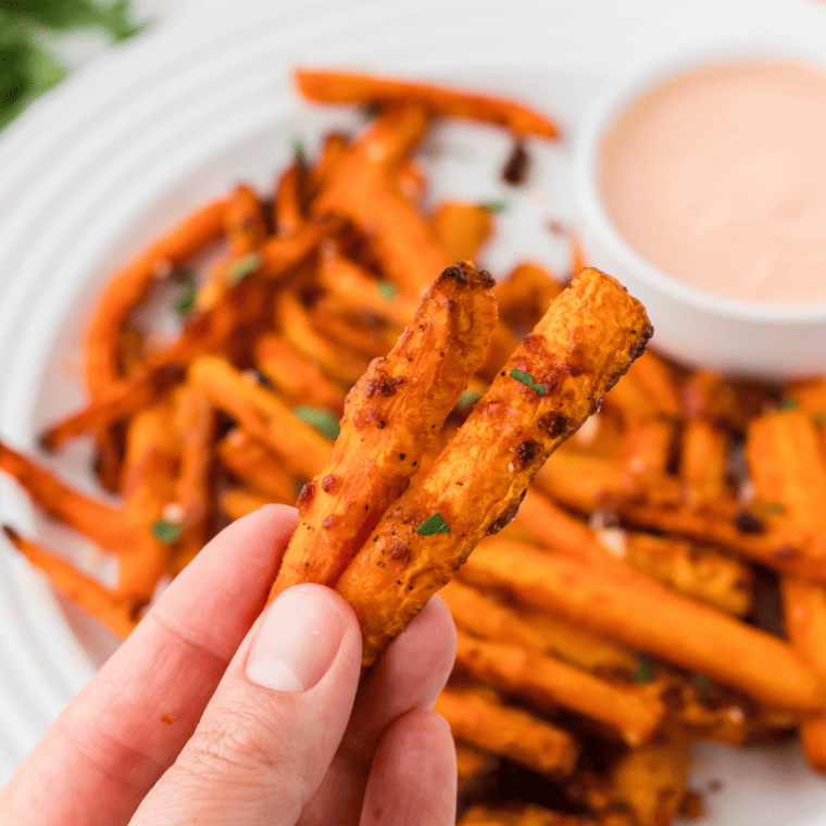 Golden, crispy air fryer carrot fries served on a plate with a side of dipping sauce.