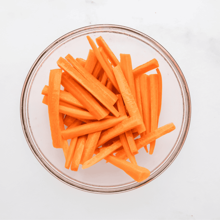 Freshly washed and peeled carrots cut into thin fry-shaped strips, ready for cooking.