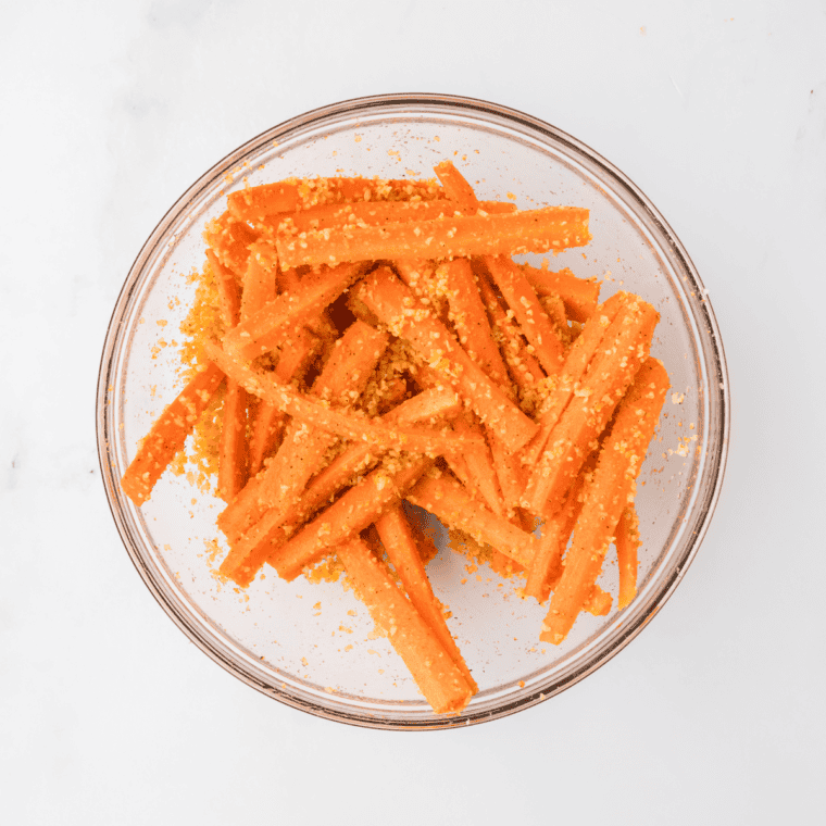 Carrot strips in a bowl, drizzled with olive oil and seasoned with salt and pepper, ready to be tossed for even coating.