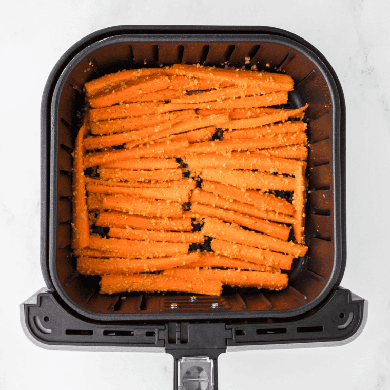 Seasoned carrot strips arranged in a single layer in the air fryer basket, cooking until crispy and golden brown.