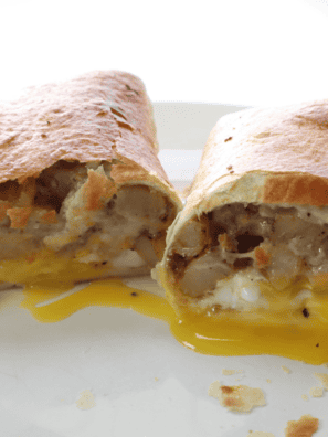 A hearty Air Fryer Barn Yard Buster Wrap filled with crispy bacon, sausage, scrambled eggs, and creamy gravy, cut in half to reveal its delicious layers.