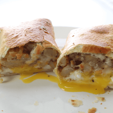 A hearty Air Fryer Barn Yard Buster Wrap filled with crispy bacon, sausage, scrambled eggs, and creamy gravy, cut in half to reveal its delicious layers.