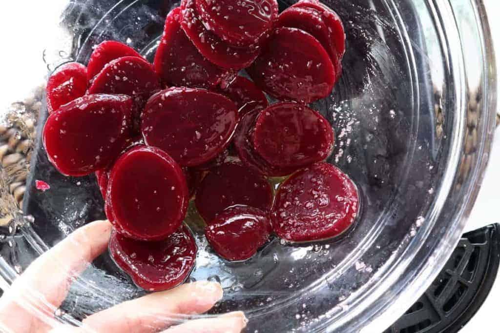 overhead: preparing beet root chips for air fryer in glass bowl with oil and seasonings