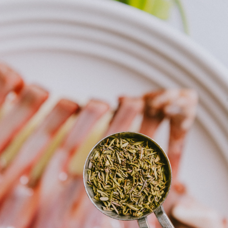 Raw lamb chops fully coated in herb marinade inside a glass dish, covered and resting in the refrigerator to absorb flavor.