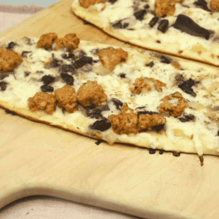 "Blackstone griddle cooking a sausage and mushroom flatbread pizza with crispy crust and melted cheese."