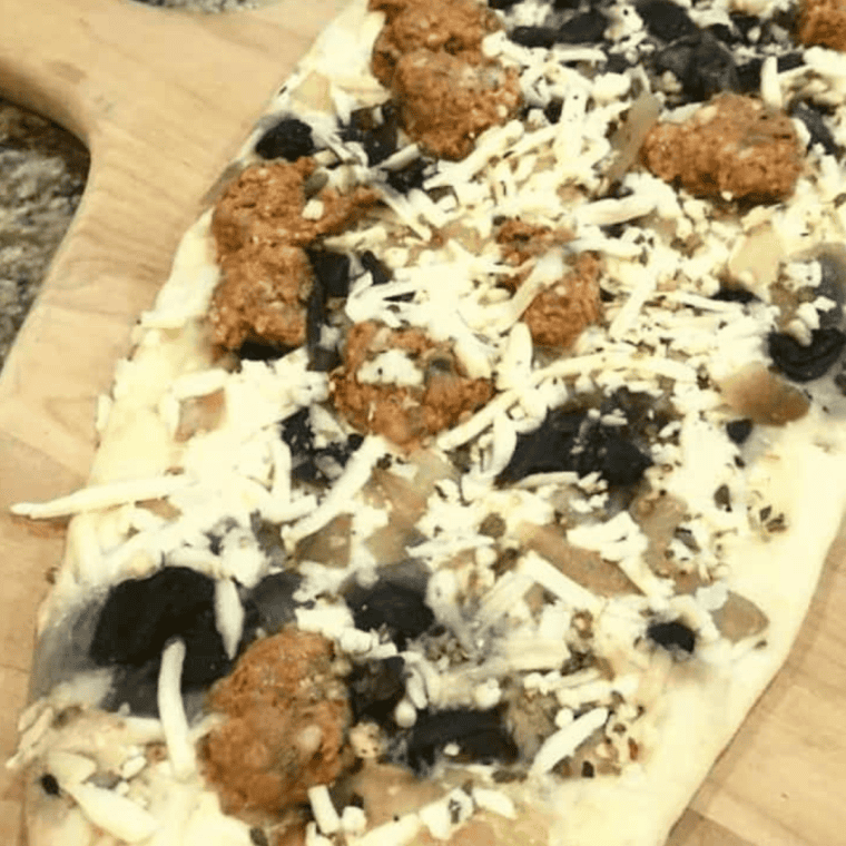 Raw flatbread pizza on cutting board.