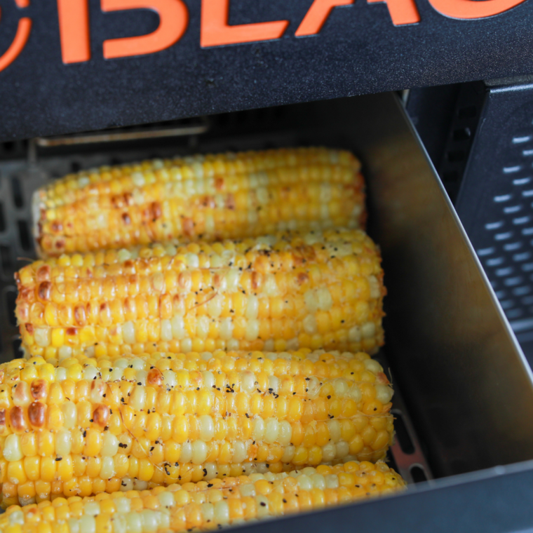 Corn on the cob cooking directly on a hot Blackstone griddle, turning evenly to achieve golden char marks on all sides, no foil used