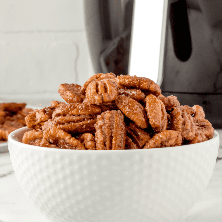 closeup side view: a white bowl full of candied pecans in air fryer