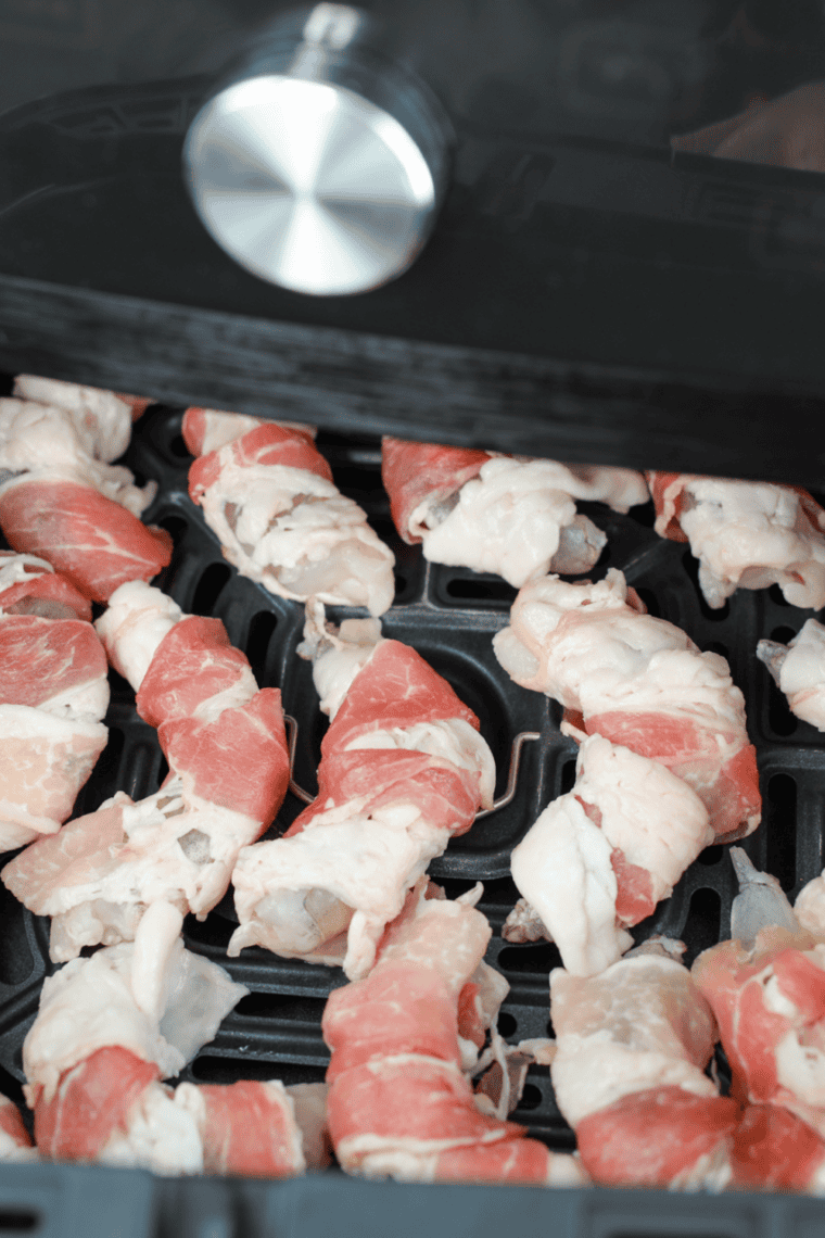Bacon-wrapped shrimp cooking in air fryer basket or oven sheet.