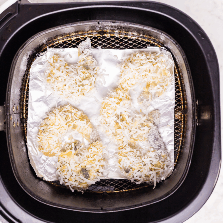 Breaded shrimp arranged in a single layer in an air fryer basket, ready to cook.