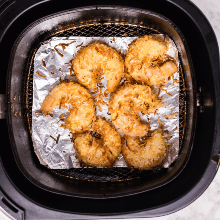 Crispy coconut shrimp served on a plate with a bowl of dipping sauce on the side.