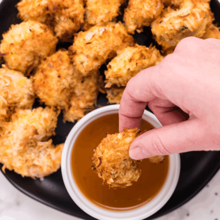Golden crispy Outback-style coconut shrimp served with a tangy dipping sauce on a white plate.