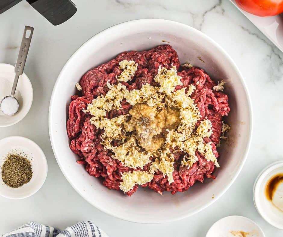 Large white bowl filled with raw beef mince, grated butter, Worcestershire Sauce, garlic, and onion powder.