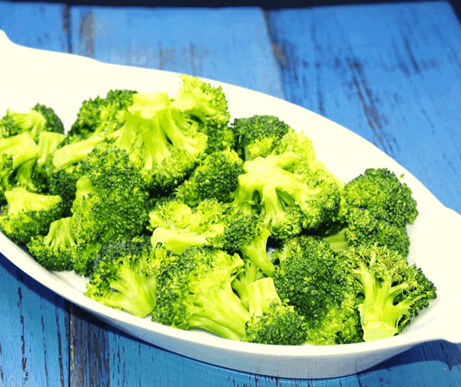 roasted broccoli florets in a white dish on a blue wooden surface