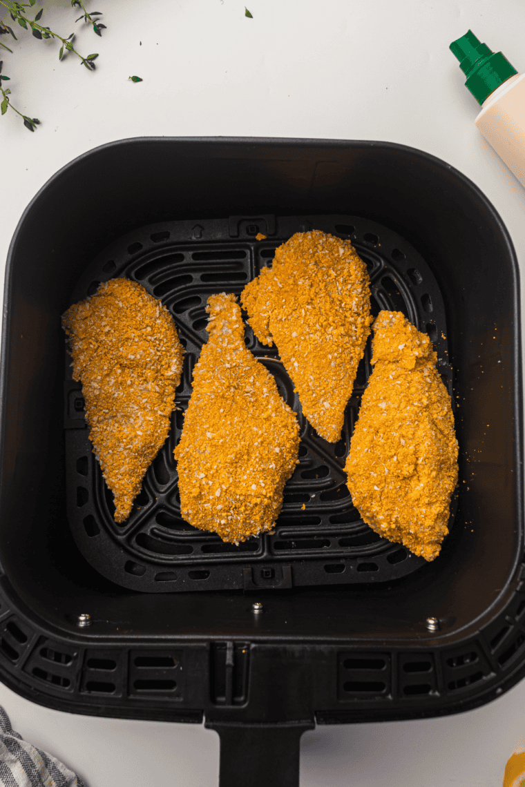 Breaded chicken cutlets placed in air fryer basket before cooking.