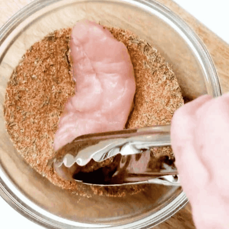 Coating chicken tenders with olive oil and seasoning mixture in a bowl.