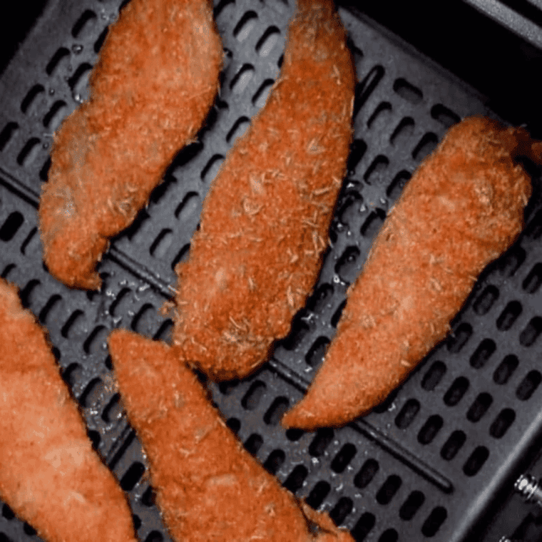 Placing seasoned chicken tenders into the air fryer basket and cooking.