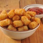 cooked tater tots in a white bowl next to a smaller bowl of ketchup