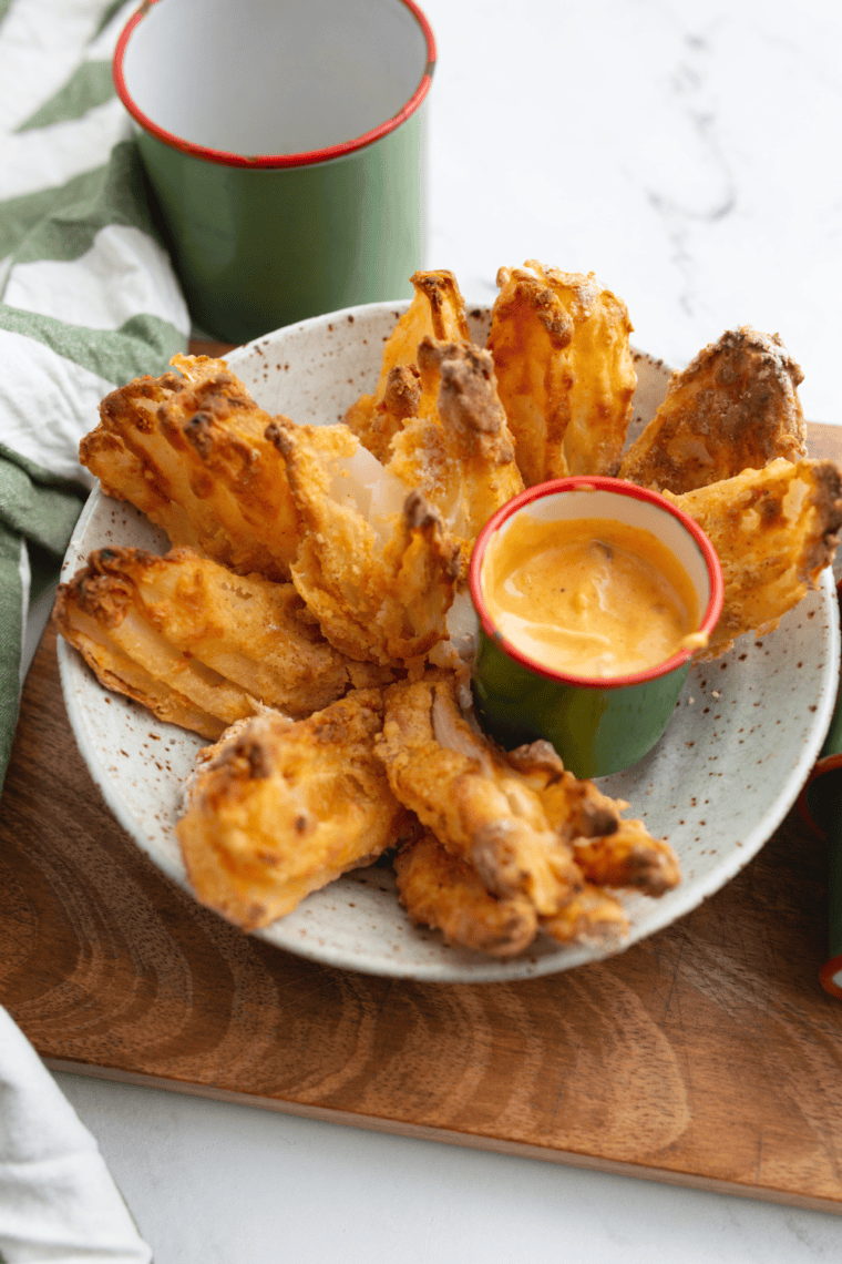 Air fryer gluten-free blooming onion with crispy golden petals, served with dipping sauce on a white plate