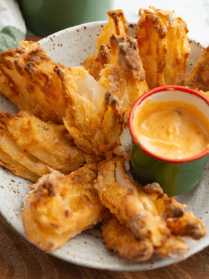 Golden brown air fryer gluten-free blooming onion with crispy seasoned coating, served with dipping sauce
