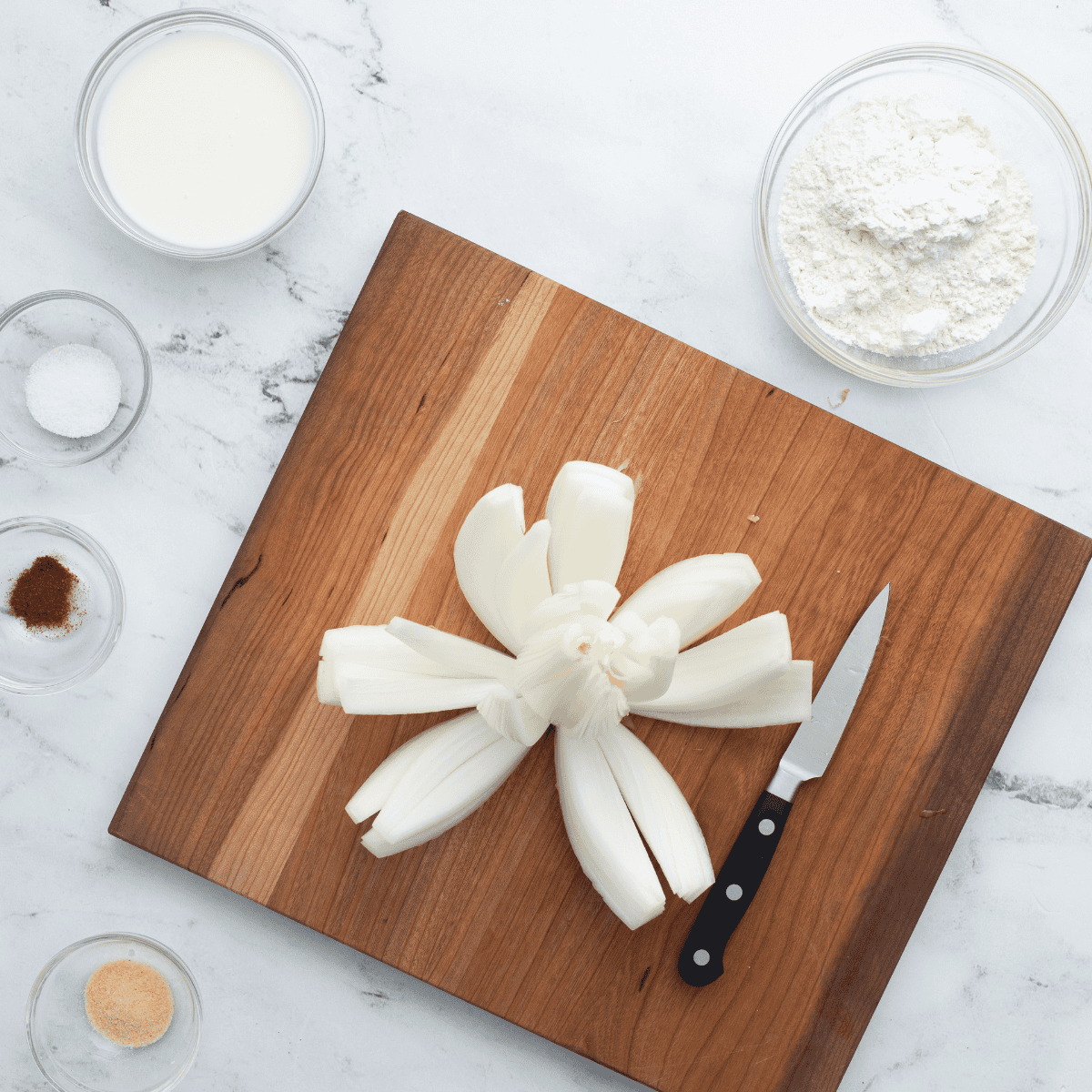 Slicing an onion into petals on a cutting board, preparing it for a blooming onion recipe