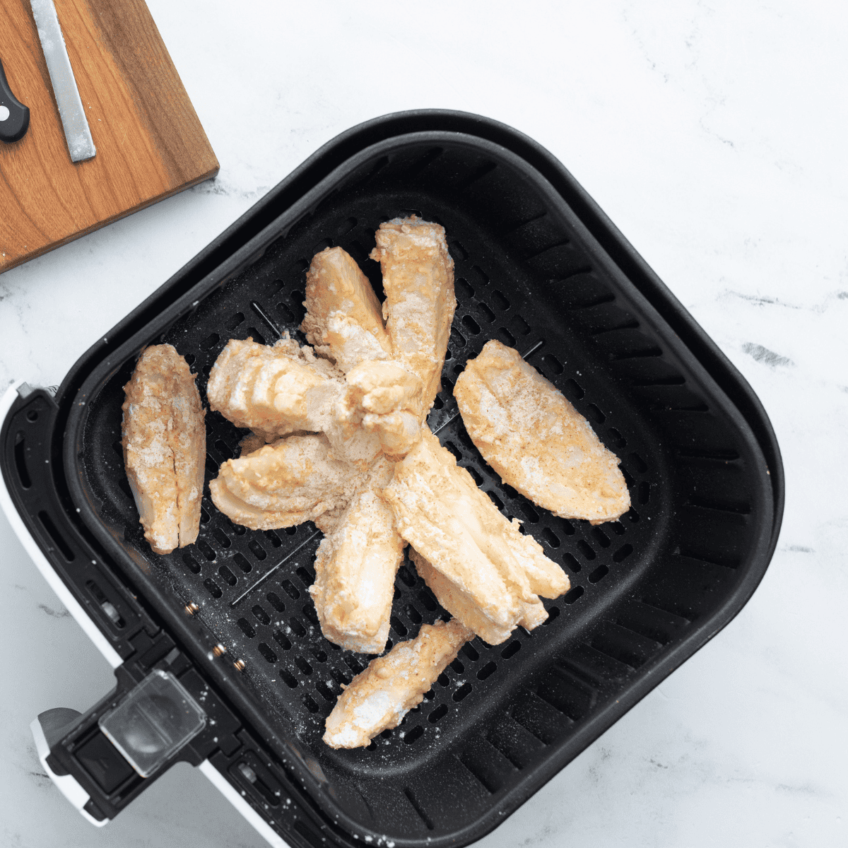 Onion placed cut-side up in air fryer basket, being sprayed with cooking spray for even crisping