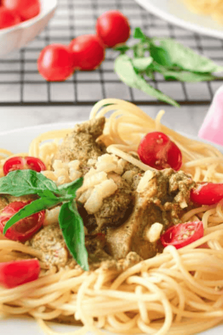 Golden pesto-coated chicken tenders cooked in the air fryer, served with fresh basil and cherry tomatoes on a plate.